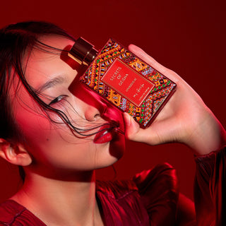 A person smelling a perfume bottle, with the bottle cap adorned with a colorful, patterned design.